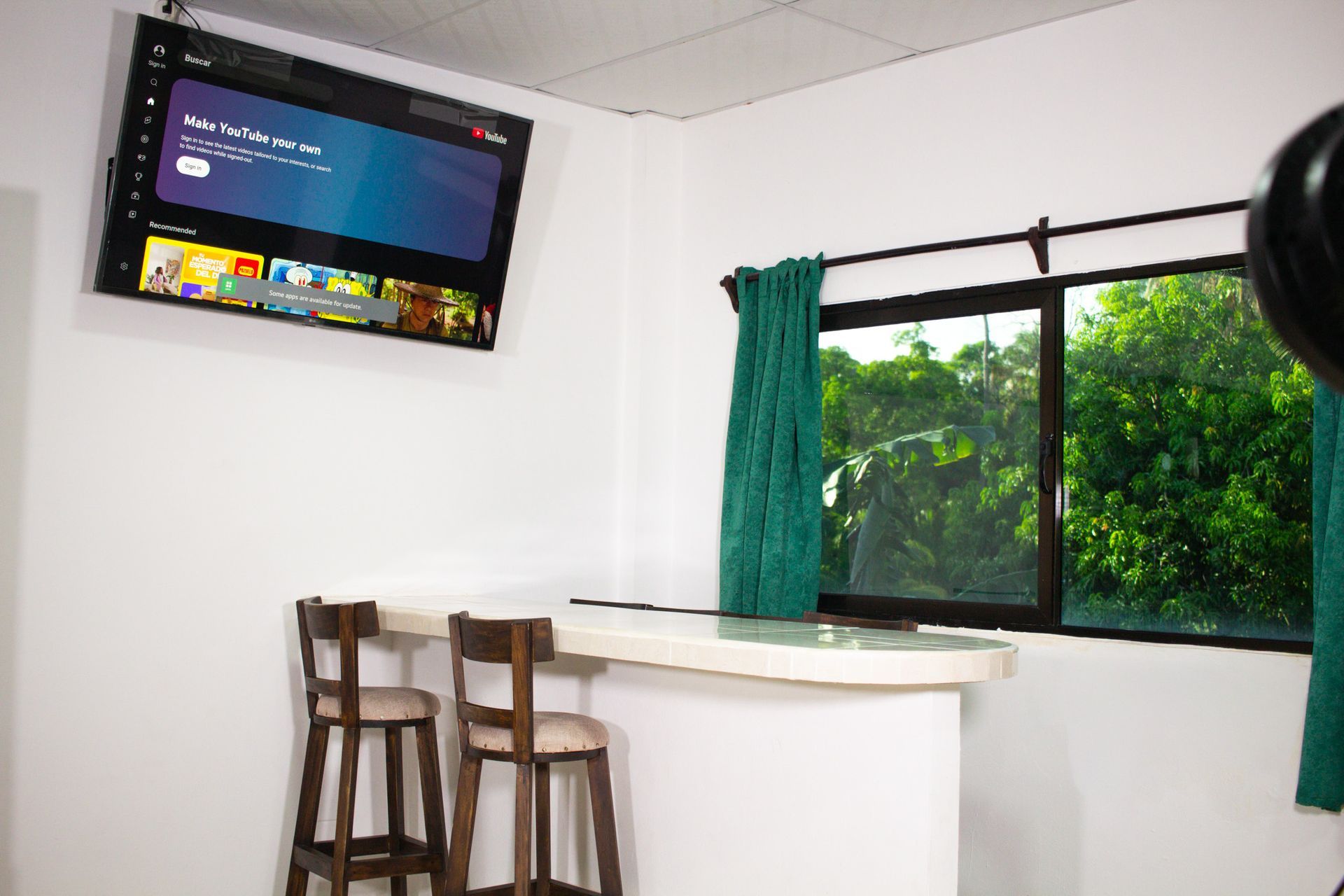 Interior room with TV, bar, stools, window, green curtains, white walls.