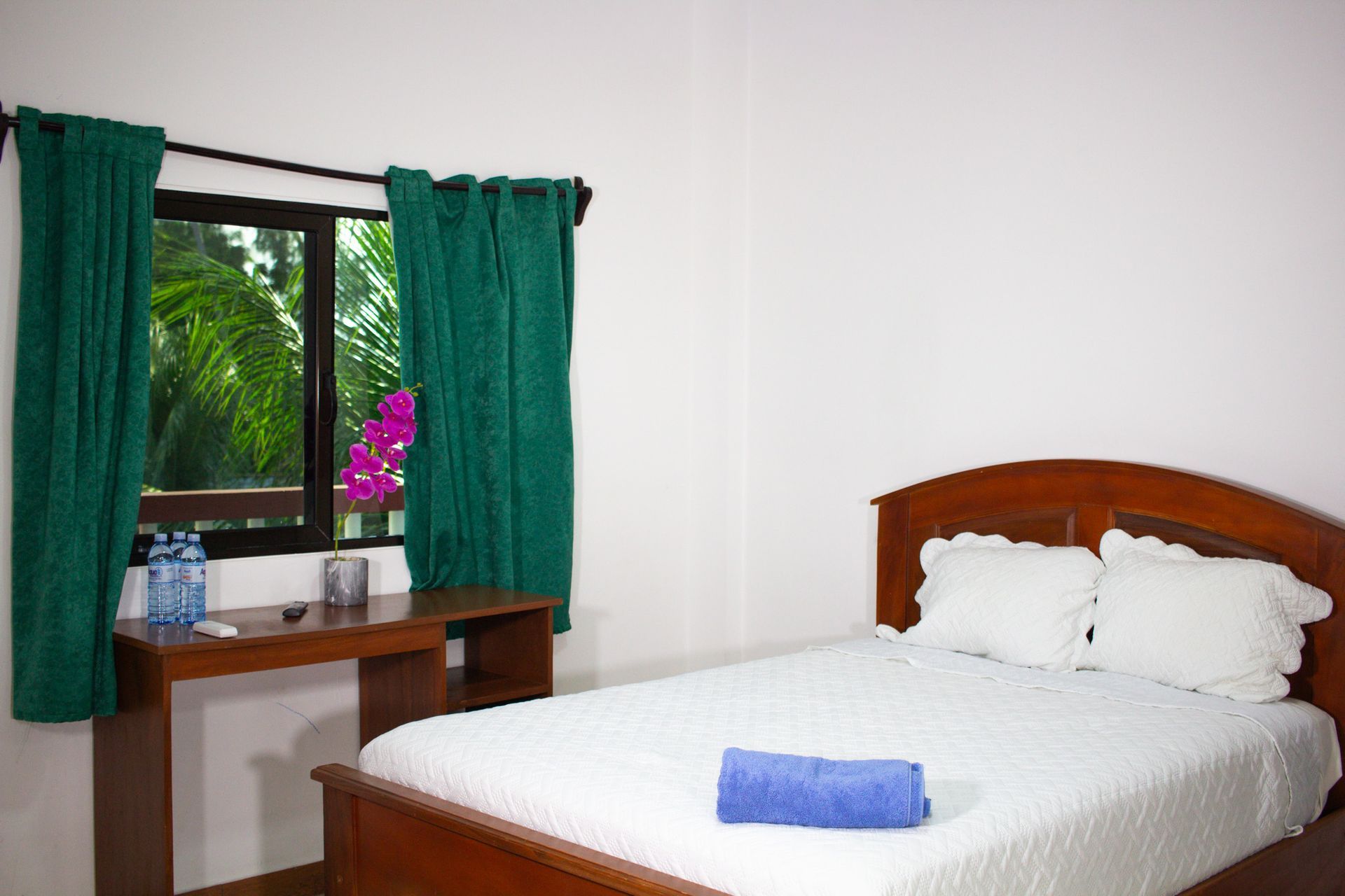 Bedroom with bed, desk, window with green curtains, and a view of greenery.