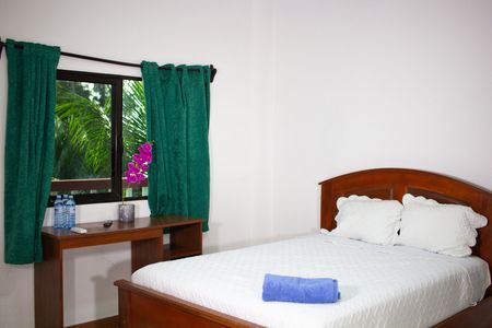 Bedroom with bed, desk, window with green curtains, and a view of greenery.