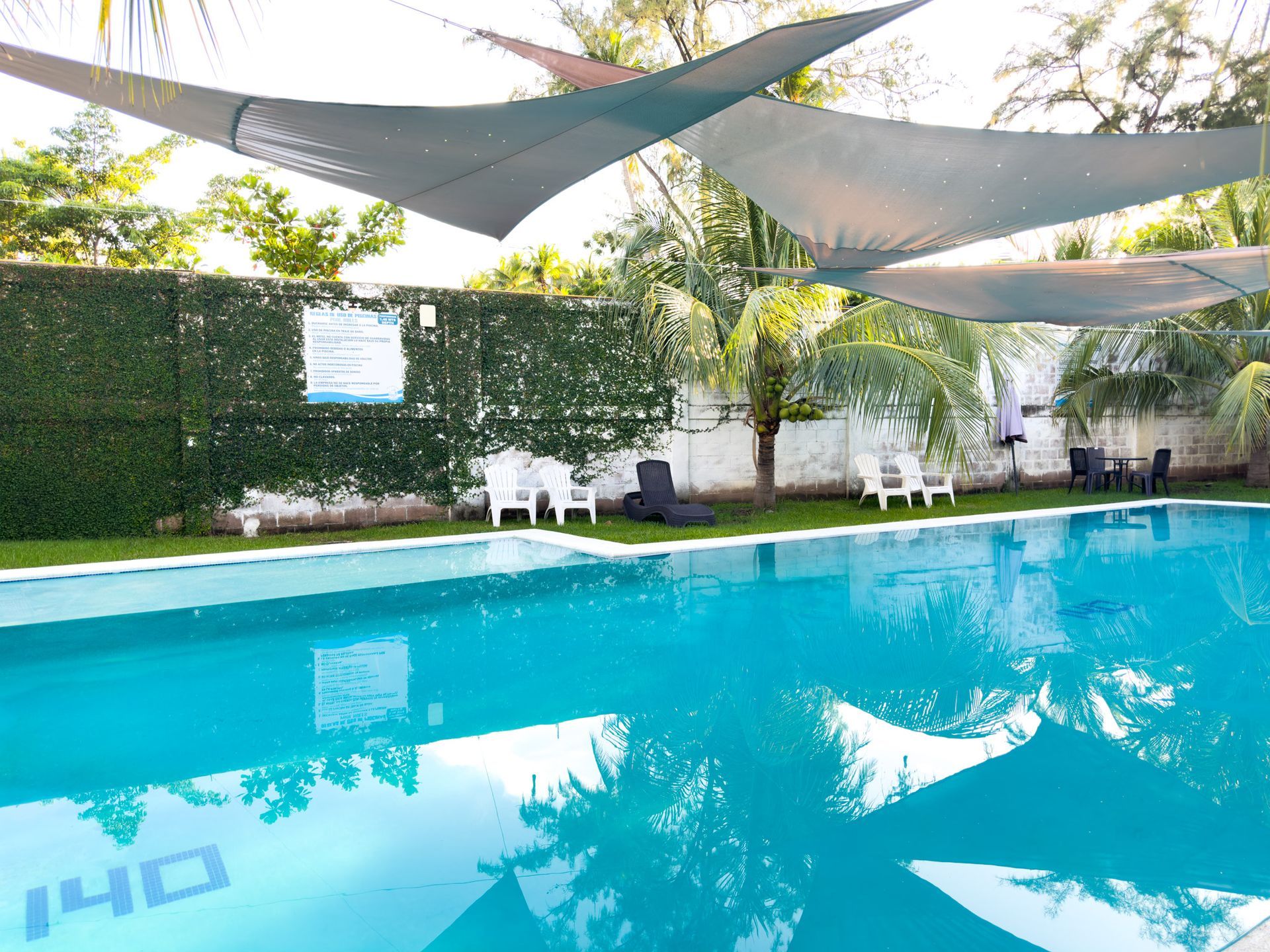Swimming pool with lounge chairs, shade sails, and a green wall.