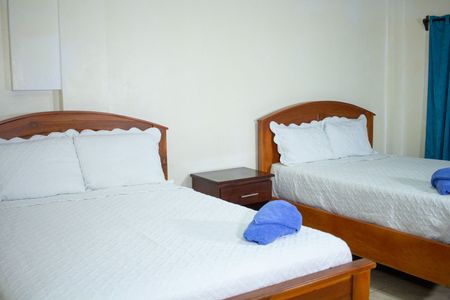 Two beds with white linens, a bedside table, and blue towels in a simple hotel room.