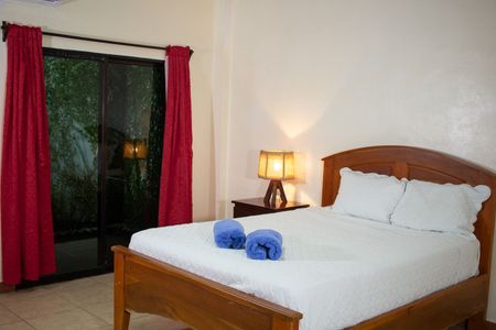 Bedroom with double bed, nightstand, sliding door with red curtains, and blue rolled towels.