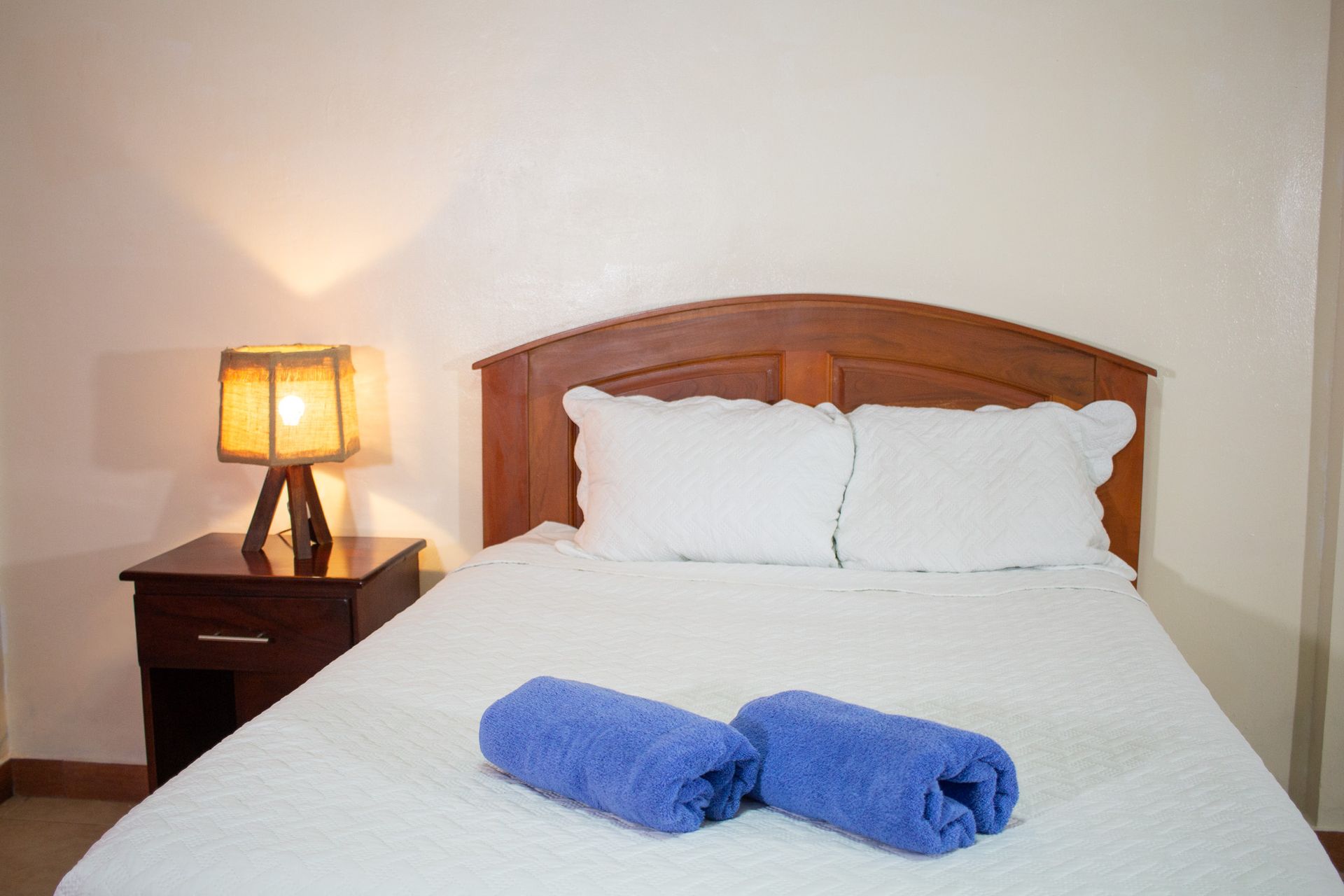 Bedroom with a double bed, nightstand, lamp, and rolled blue towels.