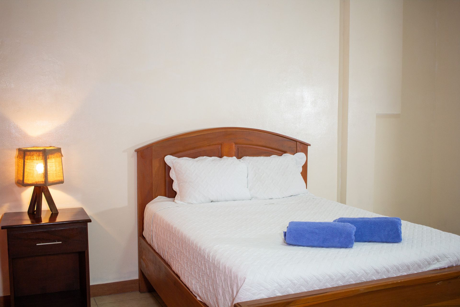 Bedroom with a wooden bed, nightstand, and lamp. Blue towels on the bed.