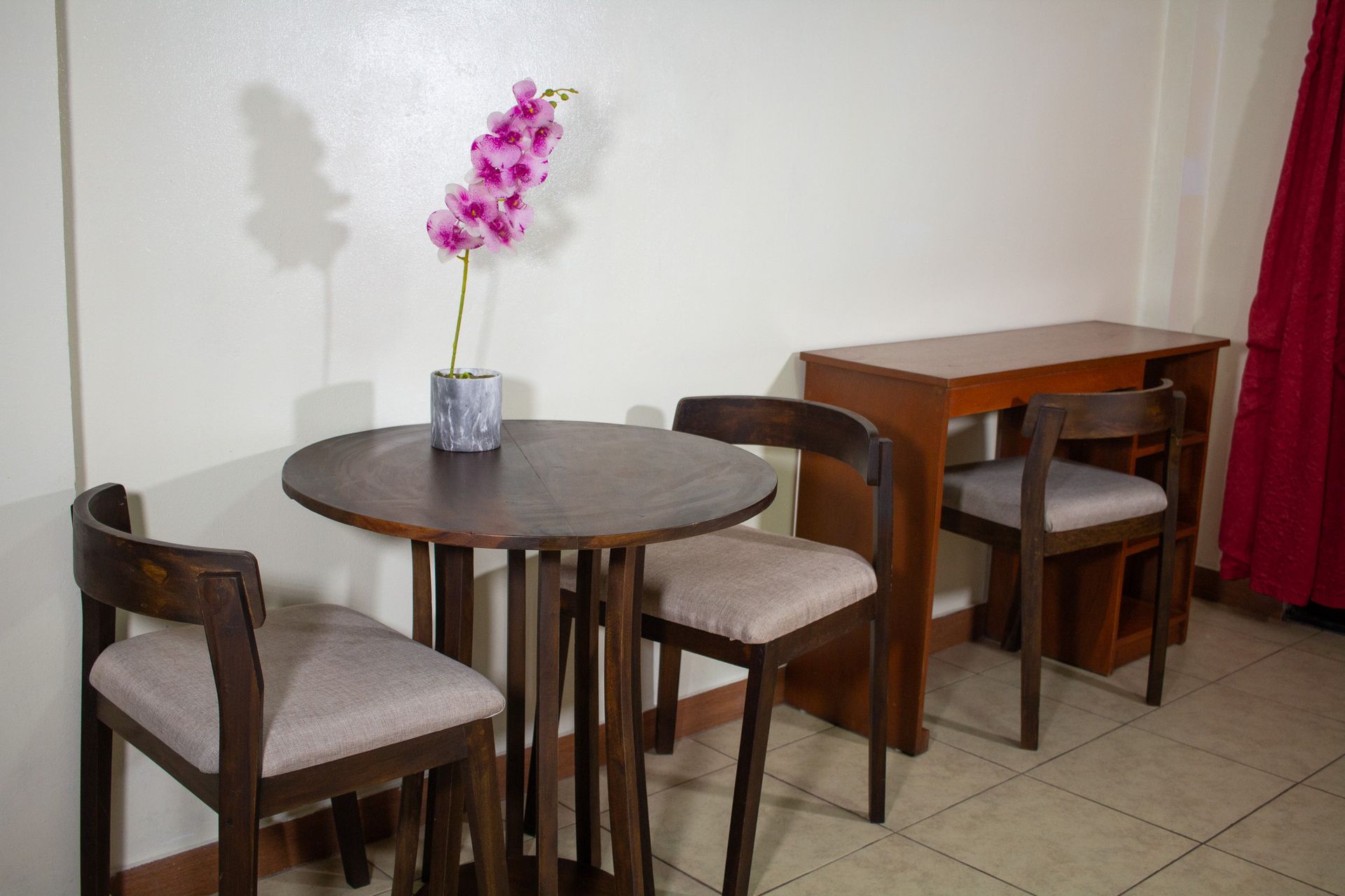Small dining area with a round table, two chairs, and a vase with pink flowers.