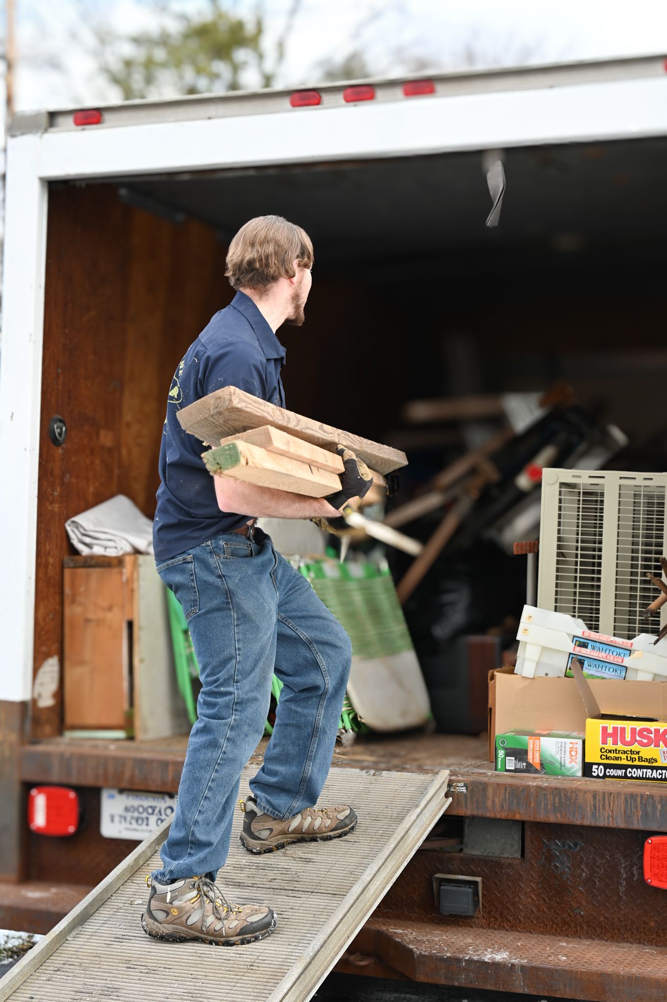A man is carrying a stack of wood from the back of a truck.