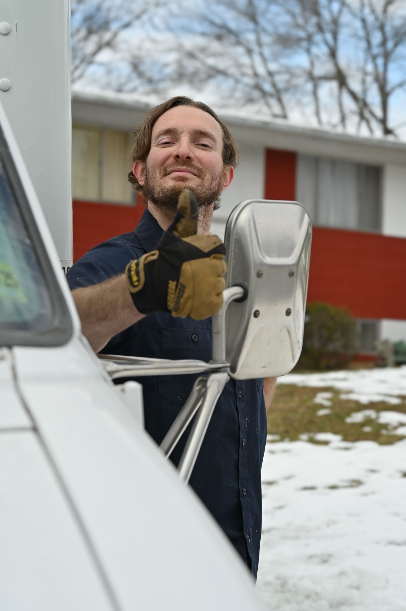 A man wearing gloves is standing next to a truck in the snow.