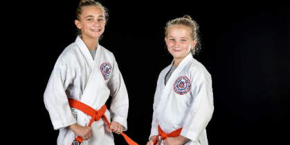 Two young girls in karate uniforms are standing next to each other.
