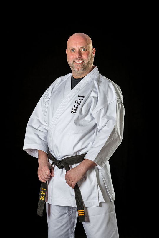 A man in a white karate uniform is holding a black belt.