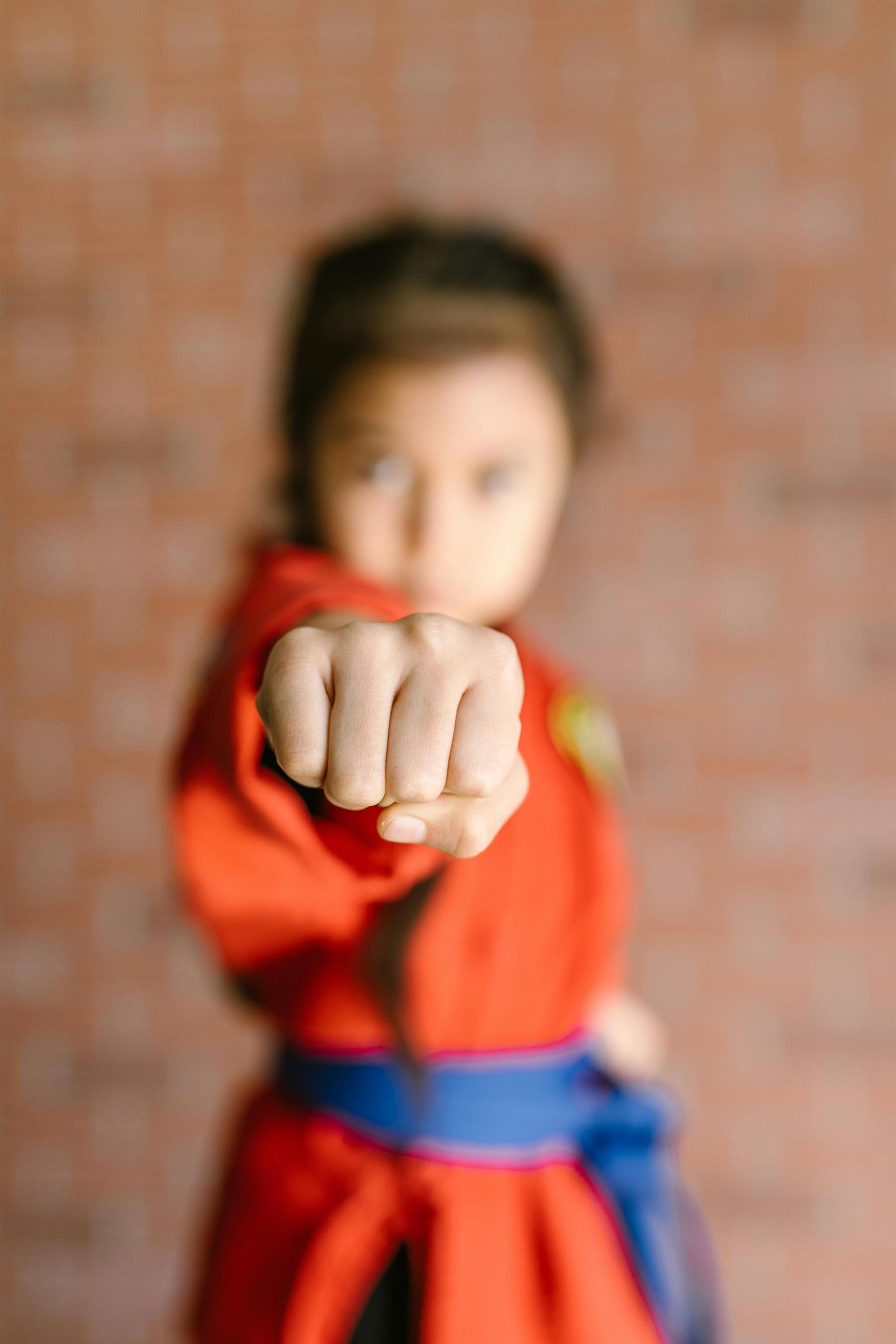 A little girl in a red karate uniform is pointing at the camera.
