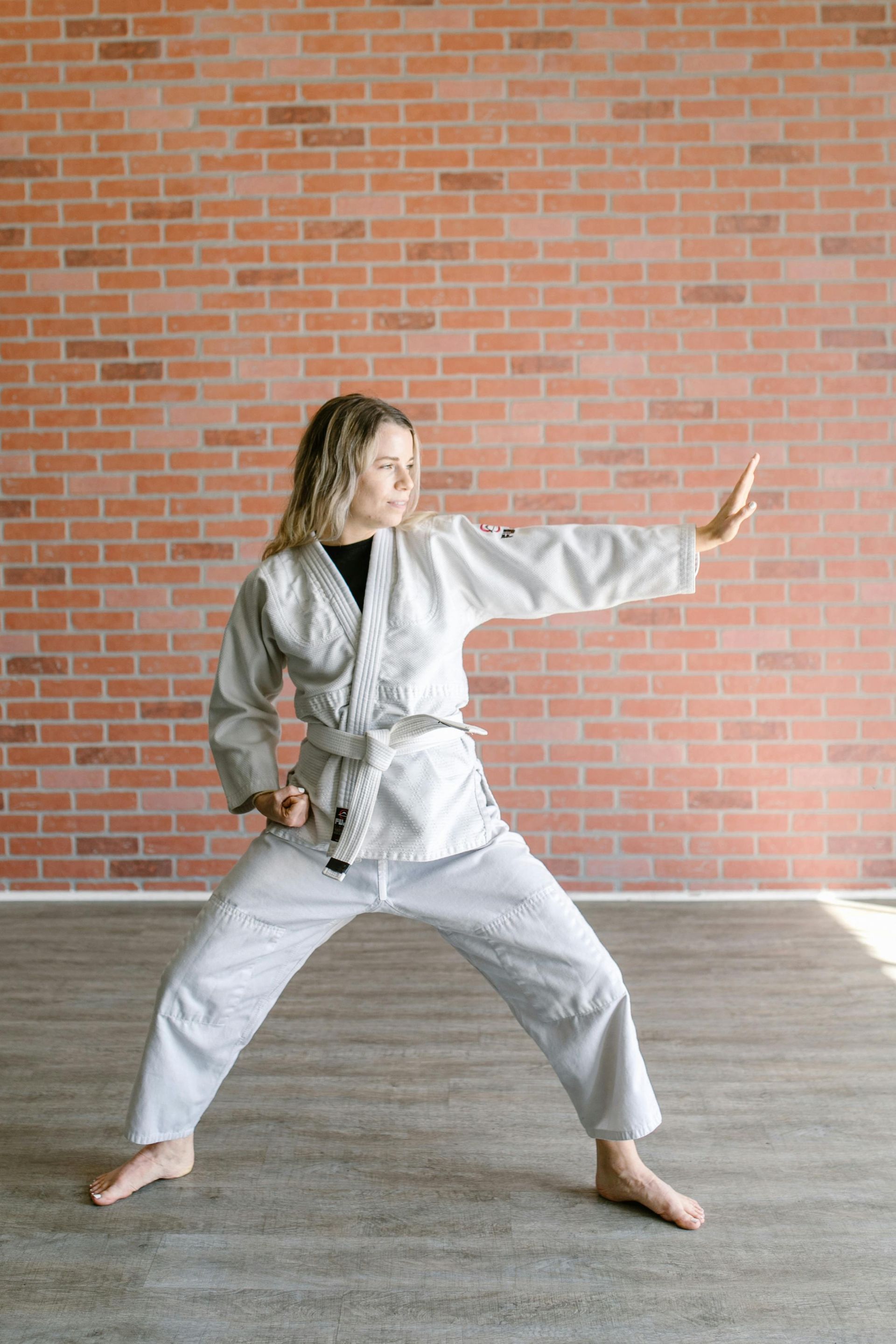 A woman in a karate uniform is practicing karate in front of a brick wall.