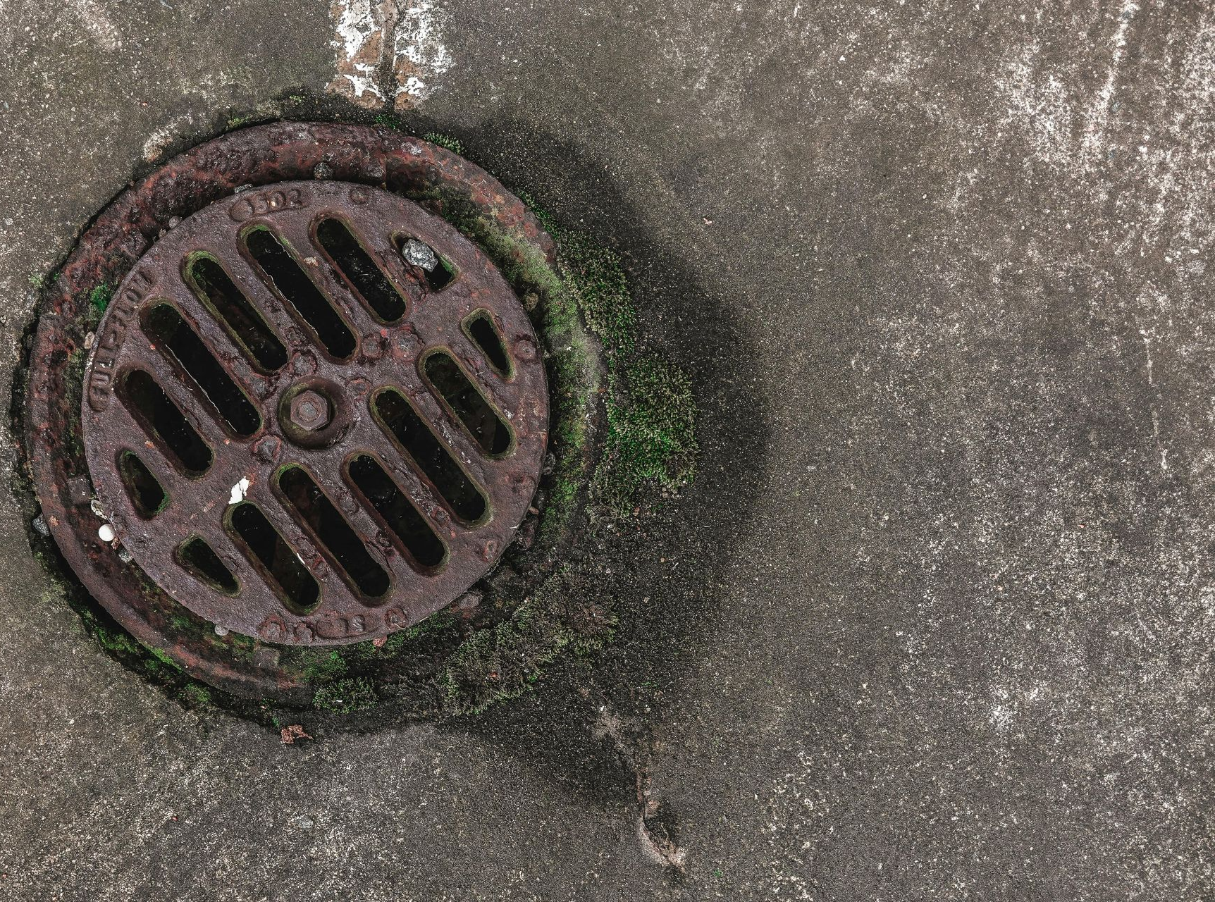 Rusty storm drain in a concrete surface, with visible moss and discoloration.