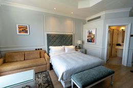 Hotel bedroom with a bed, sofa, and bathroom doorway; neutral colors.