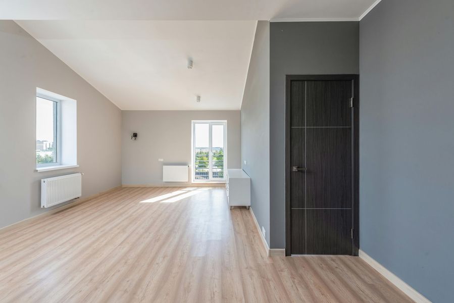 Empty room with gray walls, wooden floor, and a dark door.