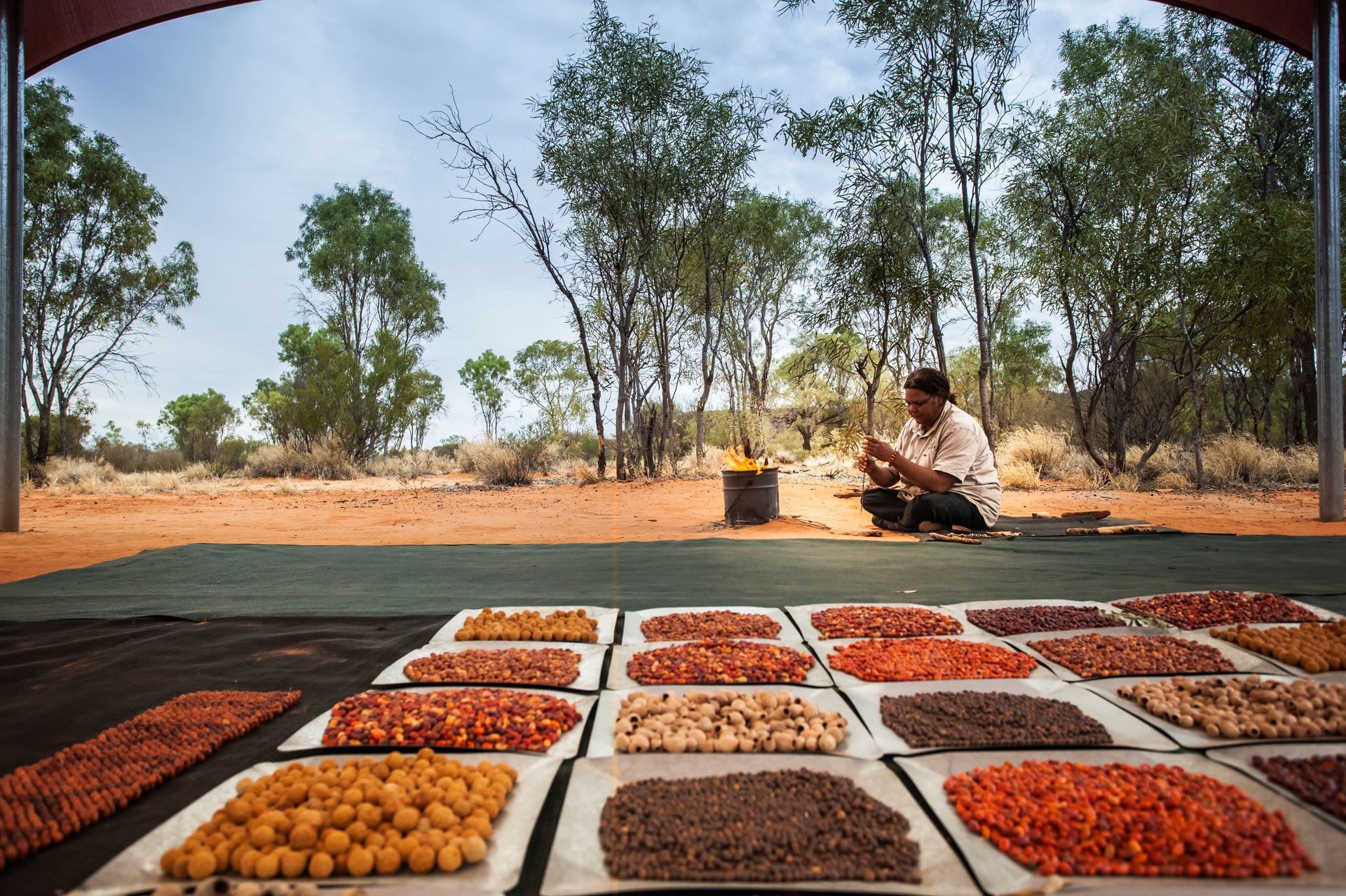A man is sitting on the ground surrounded by plates of food.