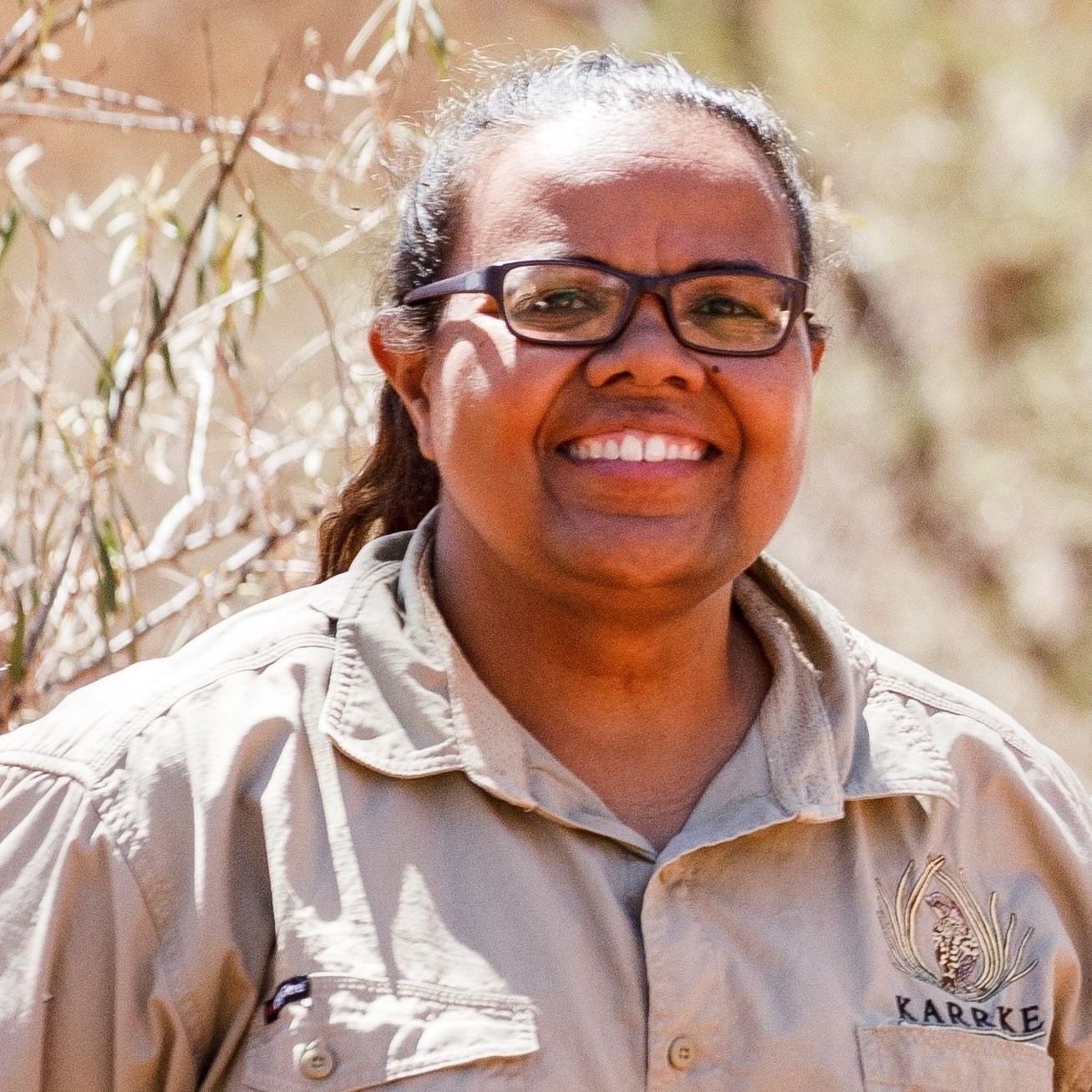 A woman wearing glasses and a khaki shirt is smiling for the camera.