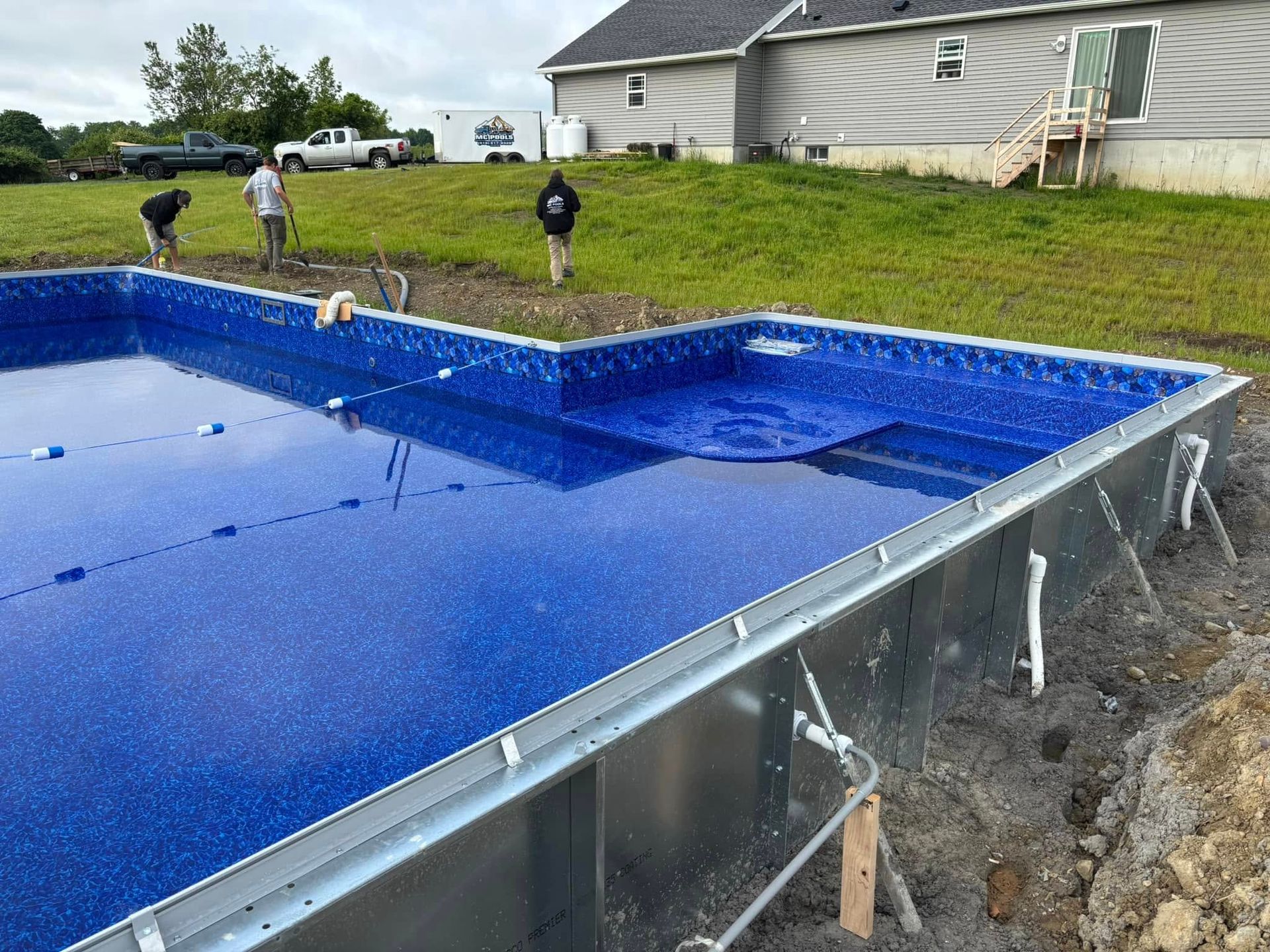 Pool under construction with workers. Blue tiled interior, metal frame, partially filled with water.