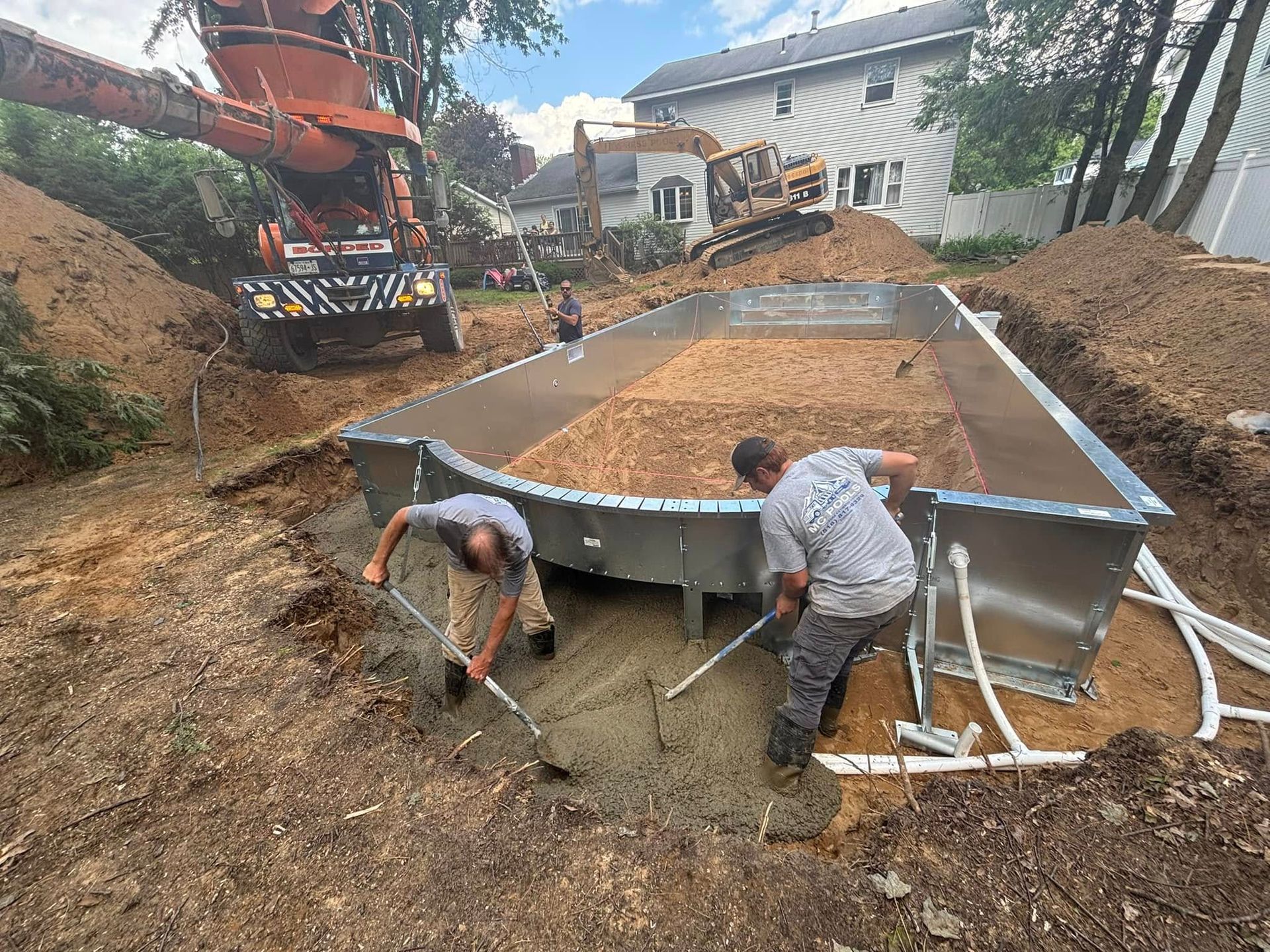 Pool construction: Workers shoveling concrete into the base of a metal pool frame.