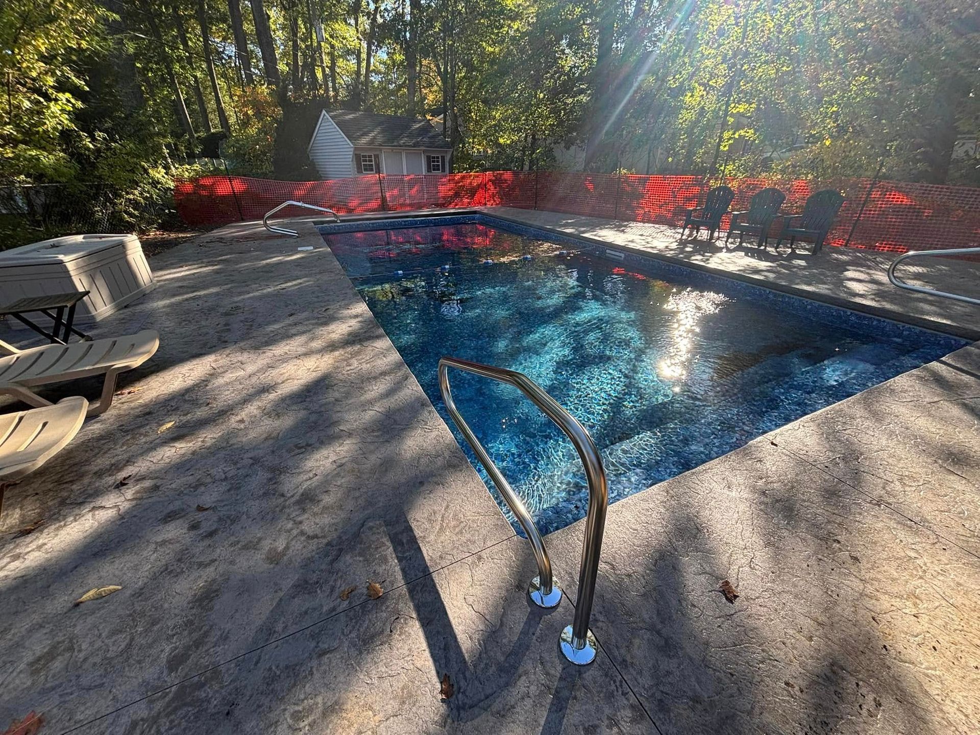 Swimming pool with blue tiles, surrounded by a concrete patio. Sunlight reflects on the water.