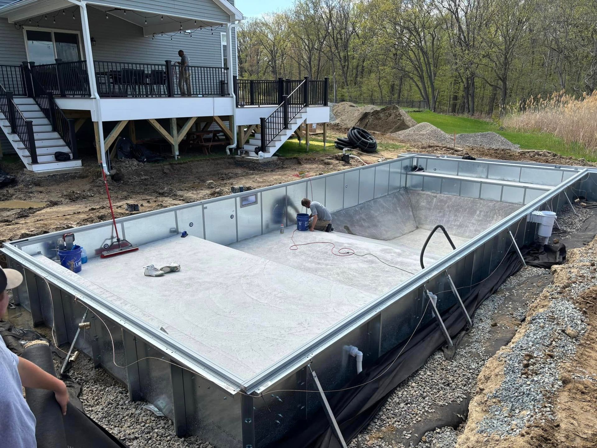 Pool construction site with a rectangular metal frame. Workers and house visible.