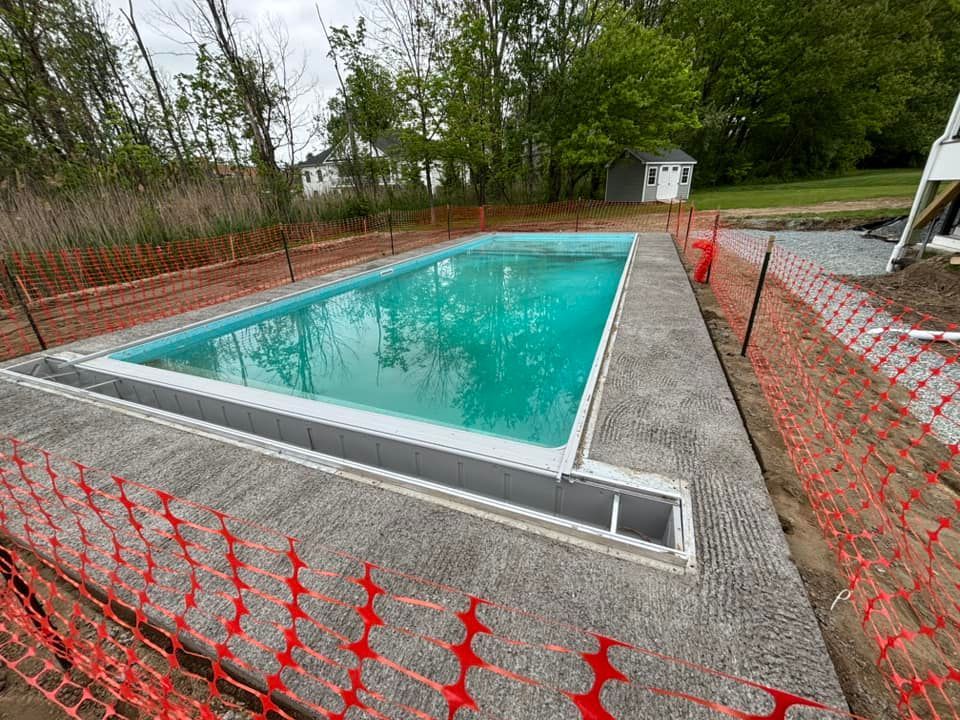 Rectangular in-ground pool surrounded by concrete and safety fencing; turquoise water.