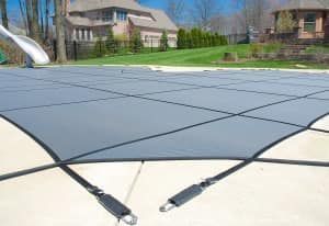 Grey pool safety cover stretched over a concrete patio; backyard with grass and houses.