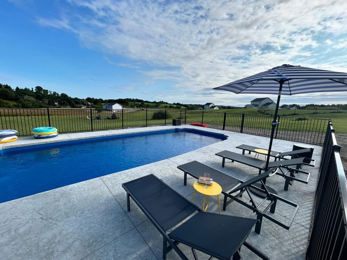 Poolside scene with pool, loungers, umbrella, and a blue sky with clouds.