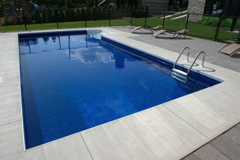 Rectangular blue swimming pool with white tile edging and a metal ladder, outdoors.