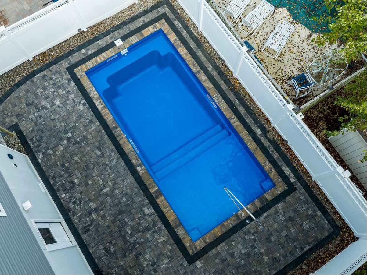Aerial view of a rectangular blue swimming pool with steps, surrounded by pavers and a white fence.