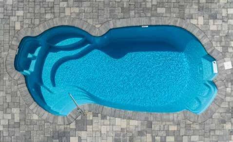 Aerial view of a blue, kidney-shaped swimming pool surrounded by a brick patio.