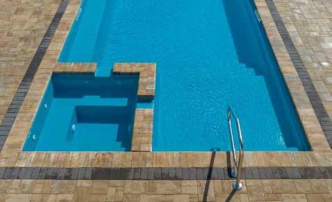 Rectangular swimming pool with attached jacuzzi, surrounded by tan and gray paving stones.