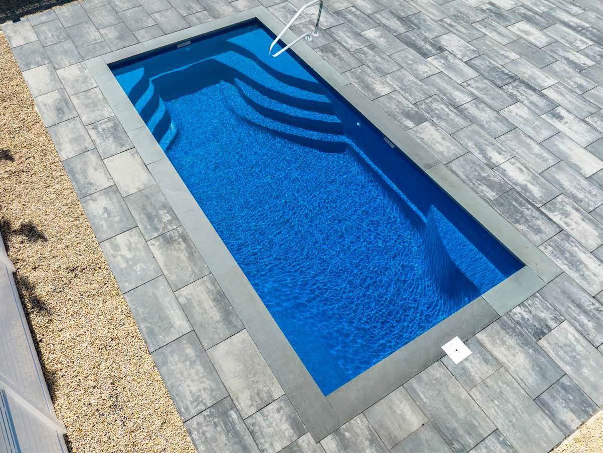 Rectangular blue swimming pool with steps, surrounded by gray paving stones.