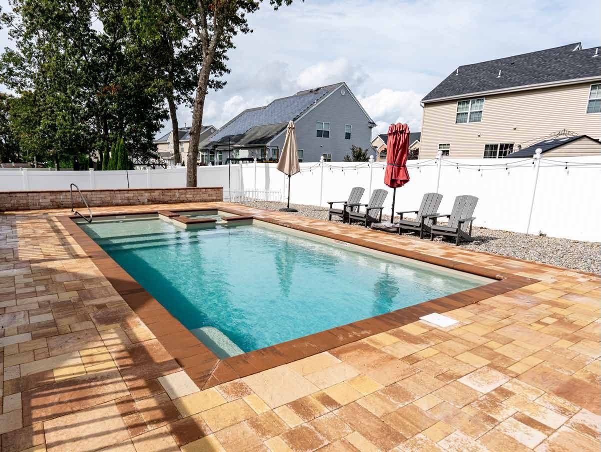 Backyard pool with brick patio, lounge chairs, umbrellas, and surrounding white fence.