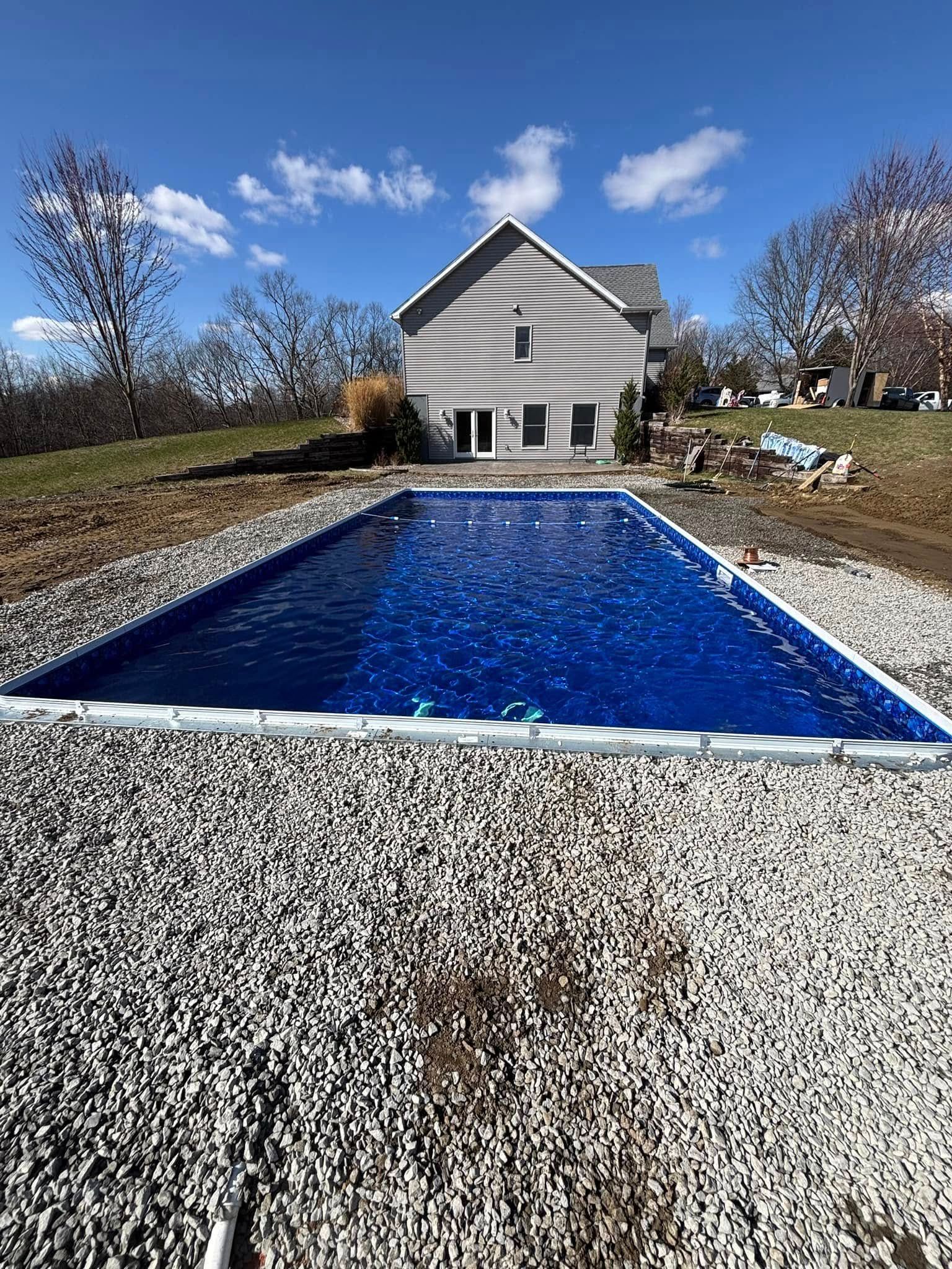 Rectangular in-ground pool surrounded by white gravel, house in the background, blue sky.