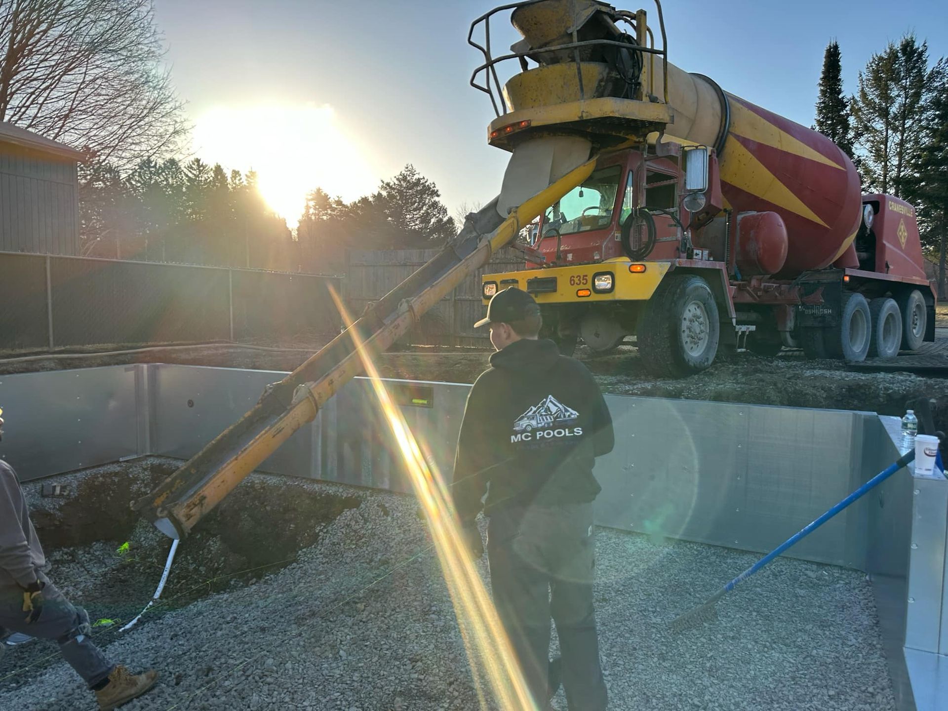 Concrete truck pouring concrete into a construction site; worker watching. Sunny day.