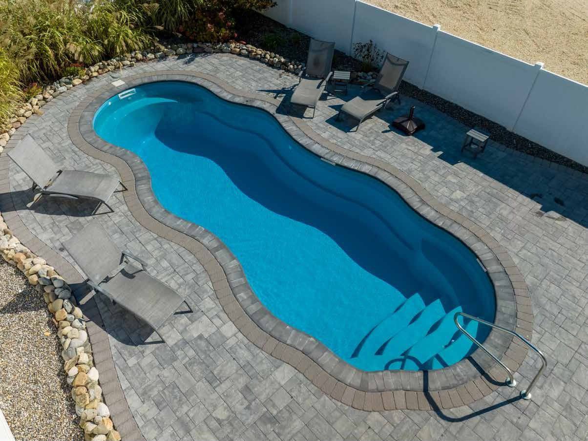 Oval-shaped swimming pool with brick patio, lounge chairs, and steps. Blue water, sunny setting.