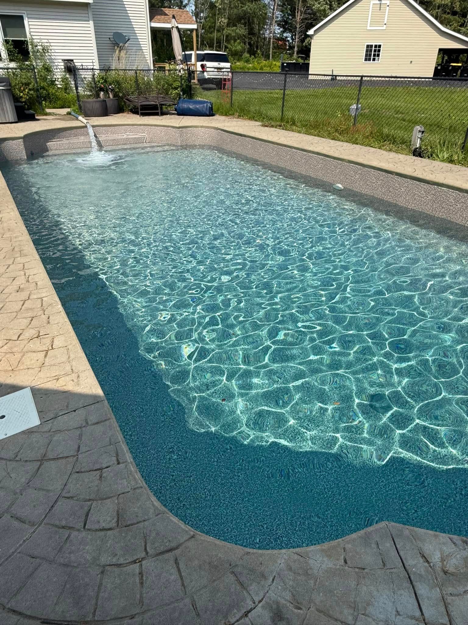 A rectangular swimming pool filled with turquoise water, surrounded by patterned stonework and greenery.