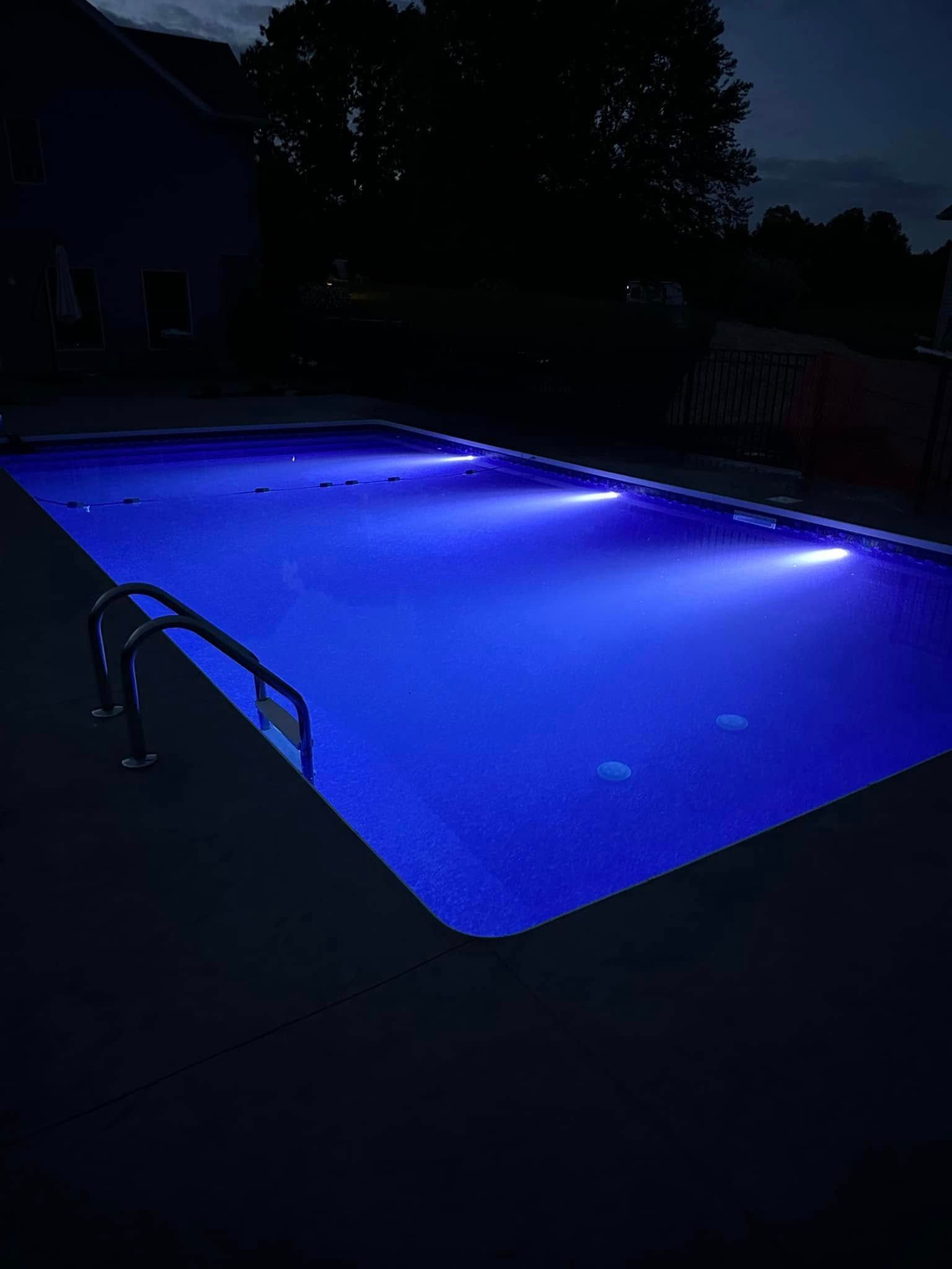 Lit blue swimming pool at night with ladder.