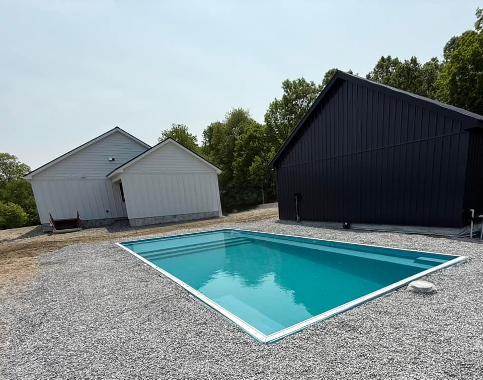 Triangular turquoise pool with white trim, set between white and black buildings on a gravel surface.