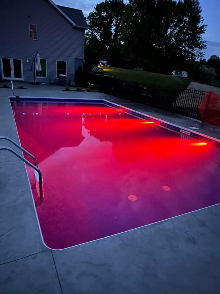 Pool illuminated with red lights at dusk. The pool is rectangular with a gray concrete patio surrounding it.