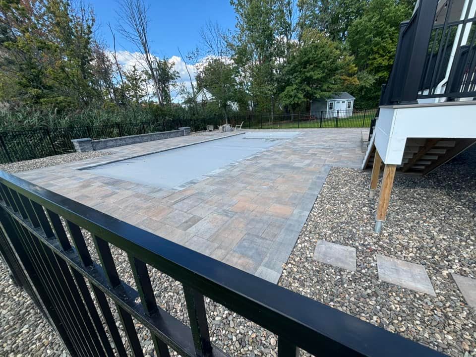 Paved patio with pool cover, black railing in foreground, steps and gravel.
