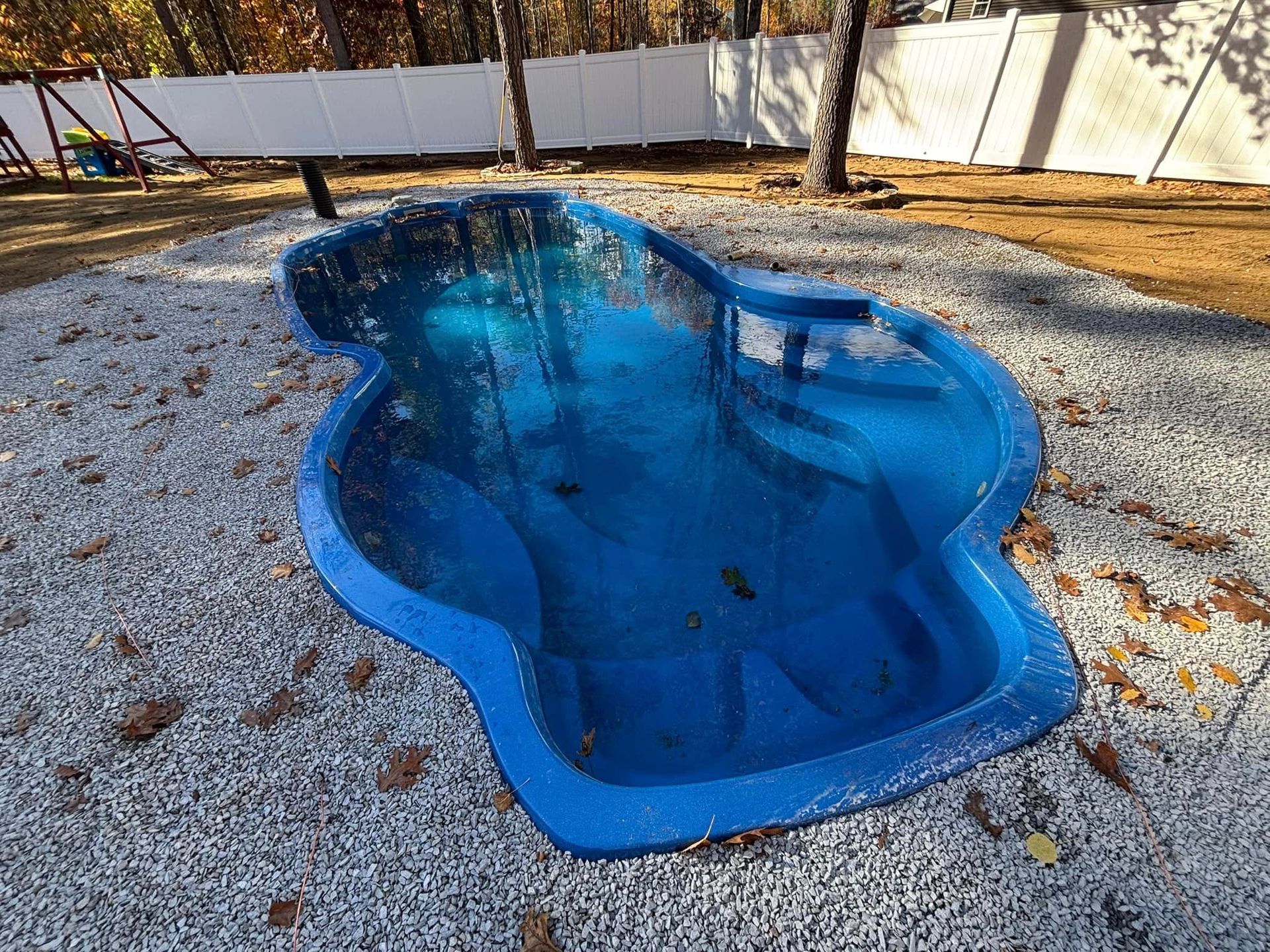 Blue, empty, kidney-shaped inground pool surrounded by gravel in a backyard.