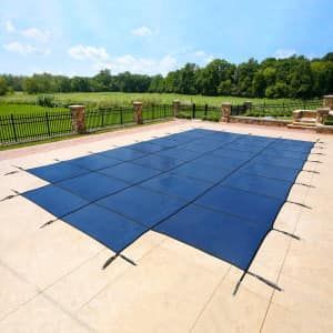Blue pool cover over a rectangular pool on a concrete patio, with a grassy background.