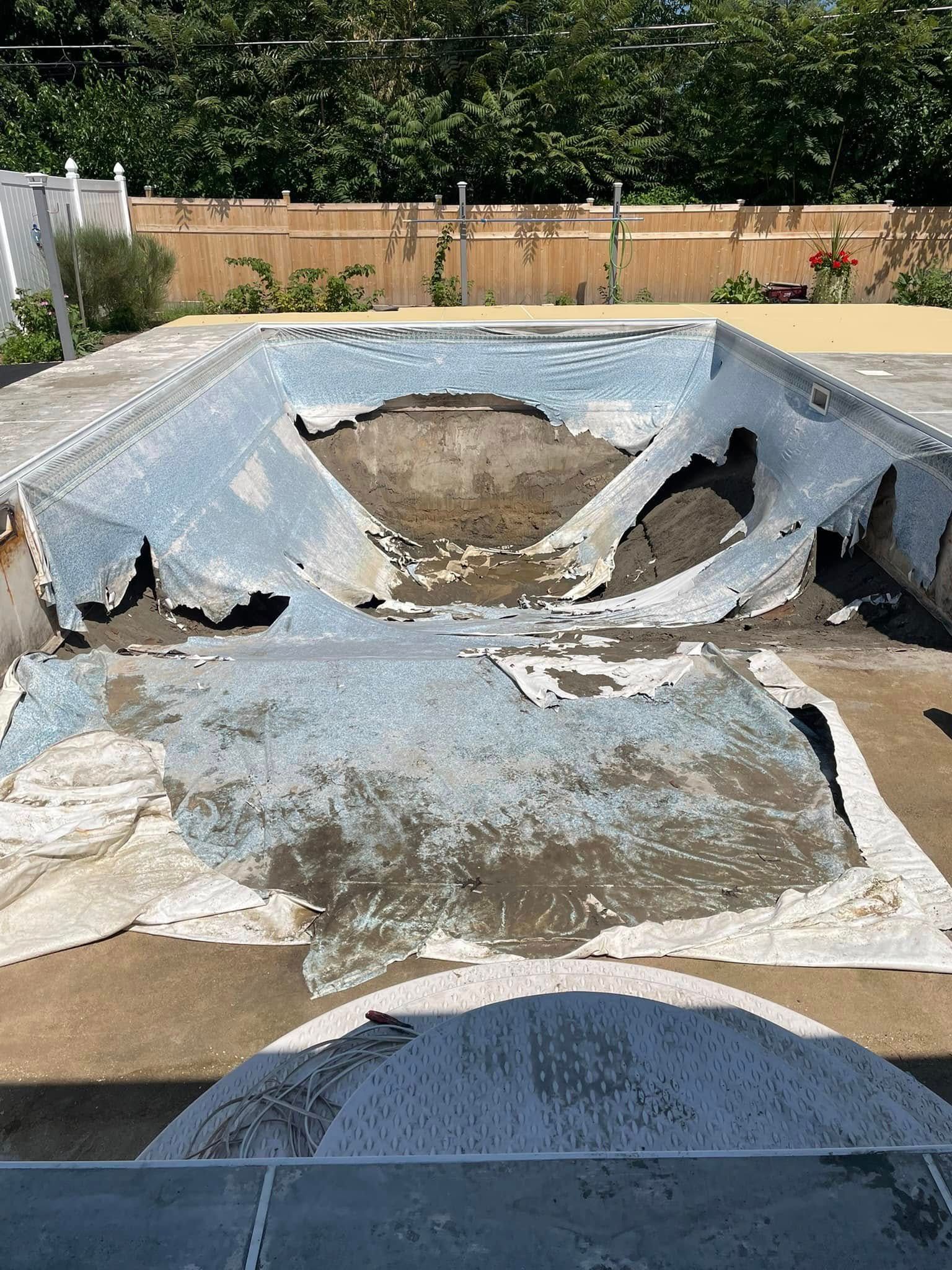 Damaged, empty swimming pool with a torn liner and surrounding concrete deck.