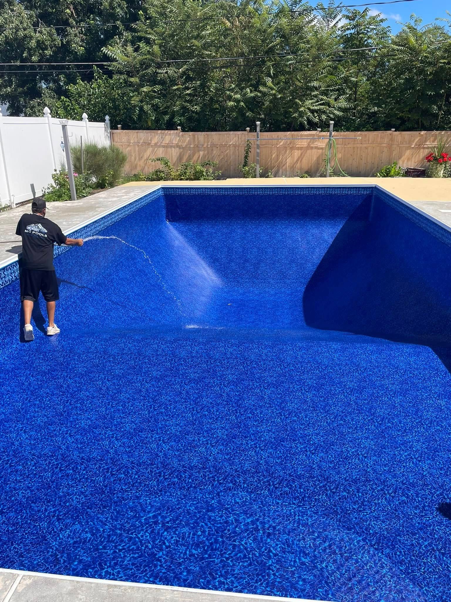 Man inspecting a newly installed blue tiled swimming pool. Outdoor setting with greenery and fence.