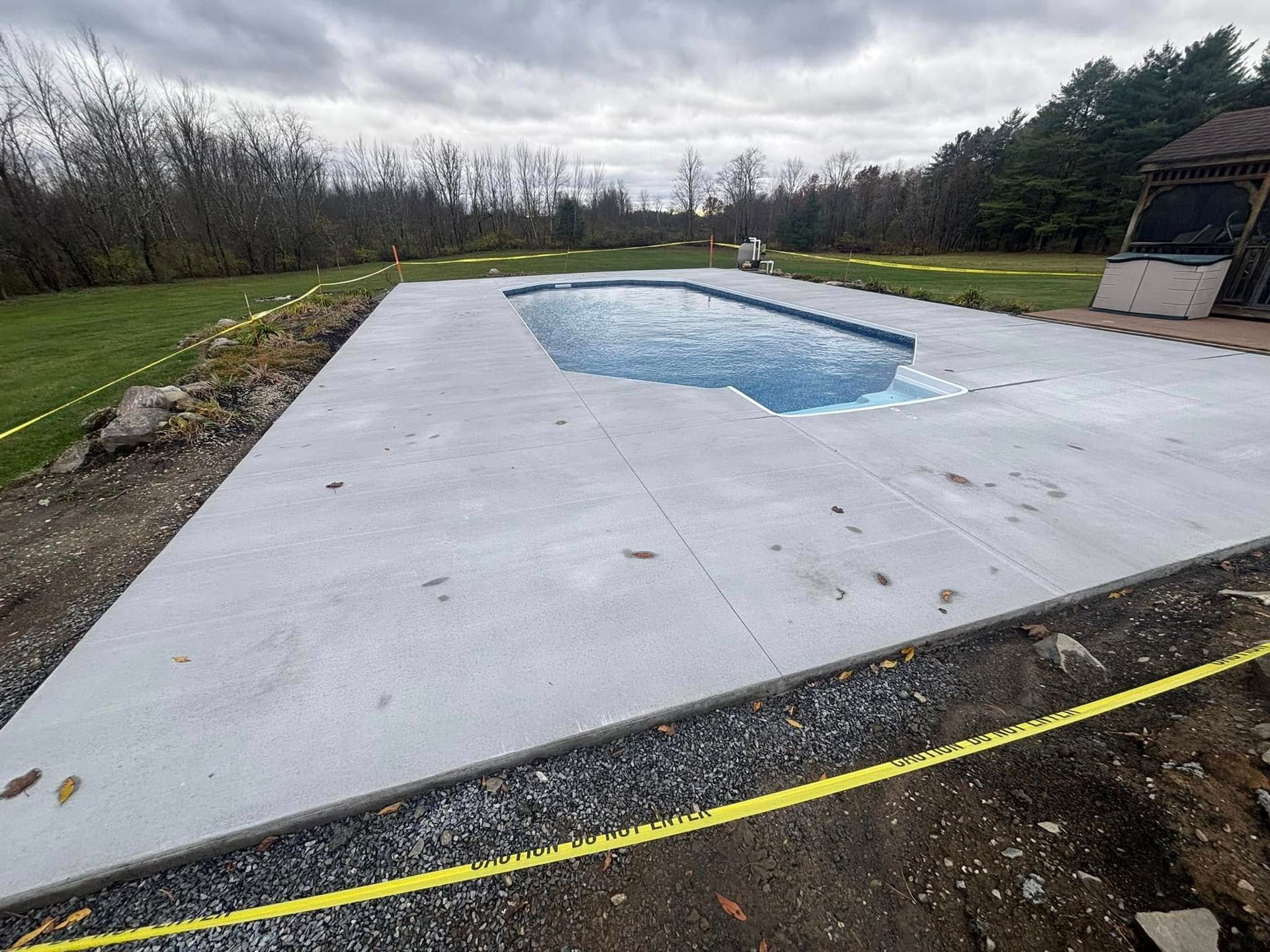 Newly constructed concrete patio with a rectangular pool. Yellow caution tape borders the edges.