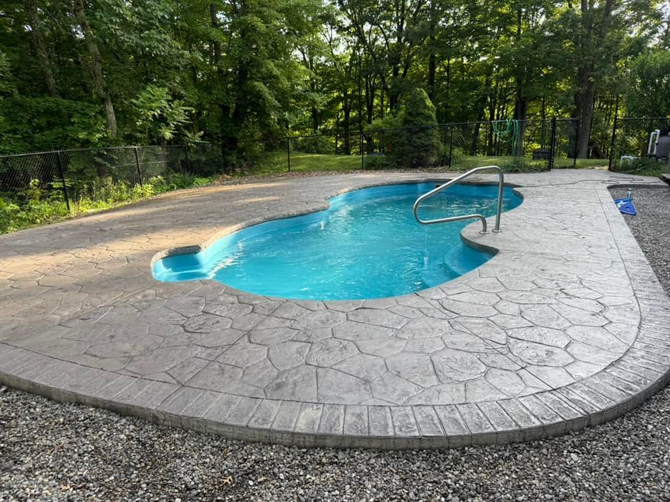 A kidney-shaped swimming pool with blue water and gray stamped concrete surround.