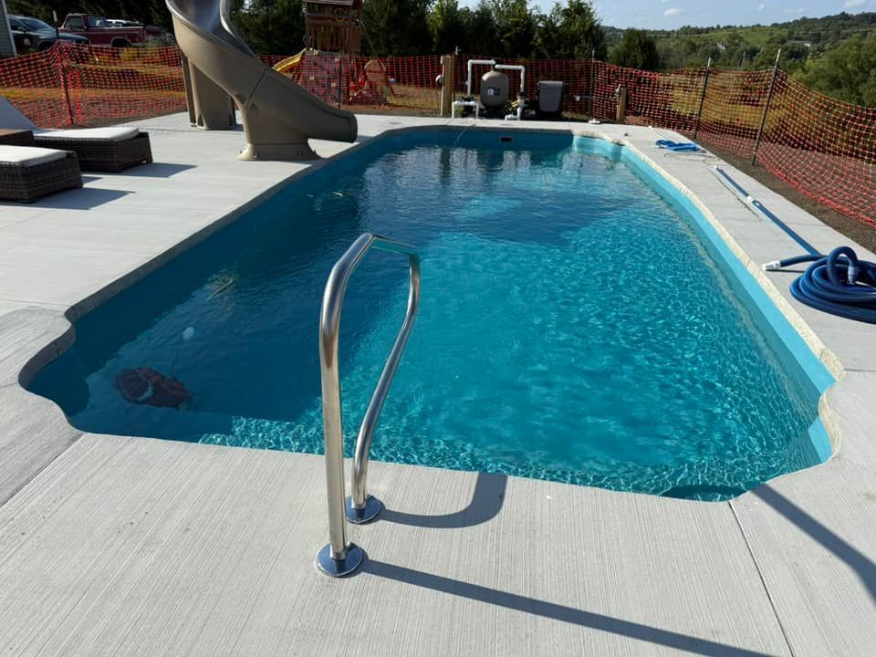 Swimming pool with blue water and stainless steel ladder; concrete deck and slide.