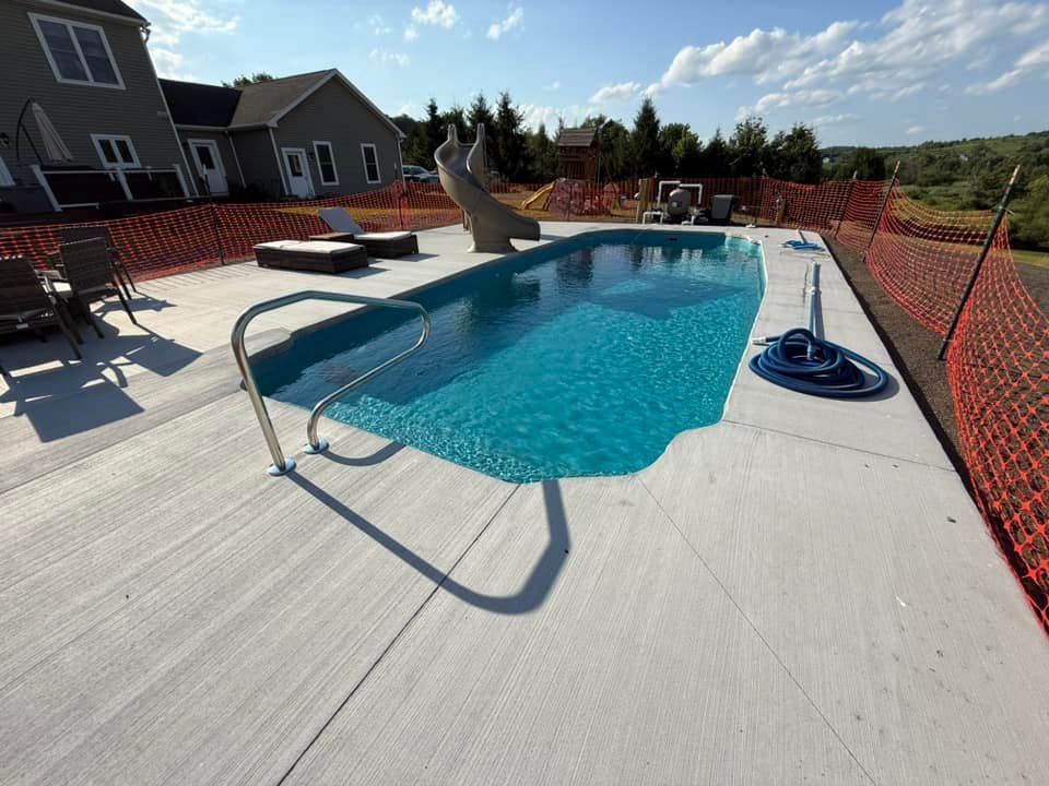 Pool with turquoise water and a slide, surrounded by a concrete patio and orange safety fencing.