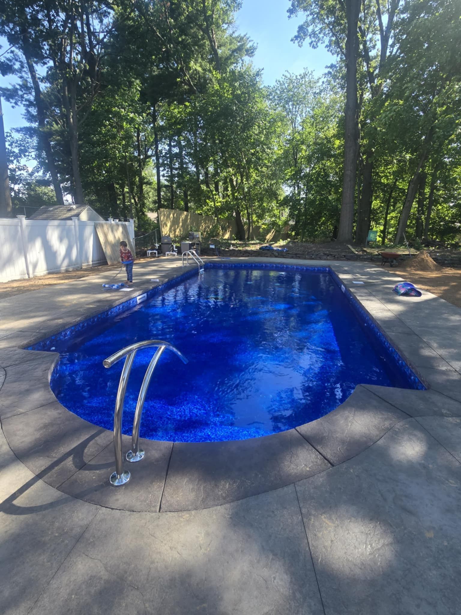 A rectangular blue swimming pool with a curved end, surrounded by concrete. Stainless steel handrails. 